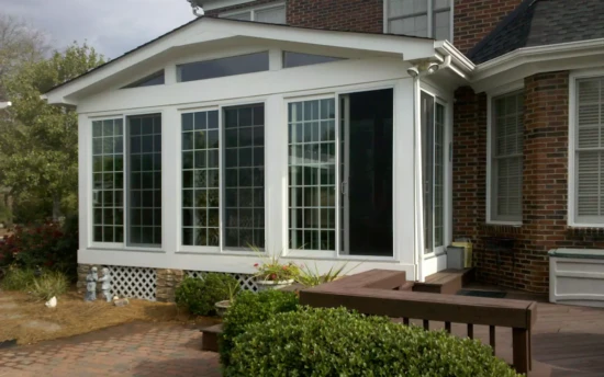 Gabled sunroom with a white aluminum frame, large grid-patterned sunroom windows, transom windows for extra light, and a sliding glass door for easy access.
