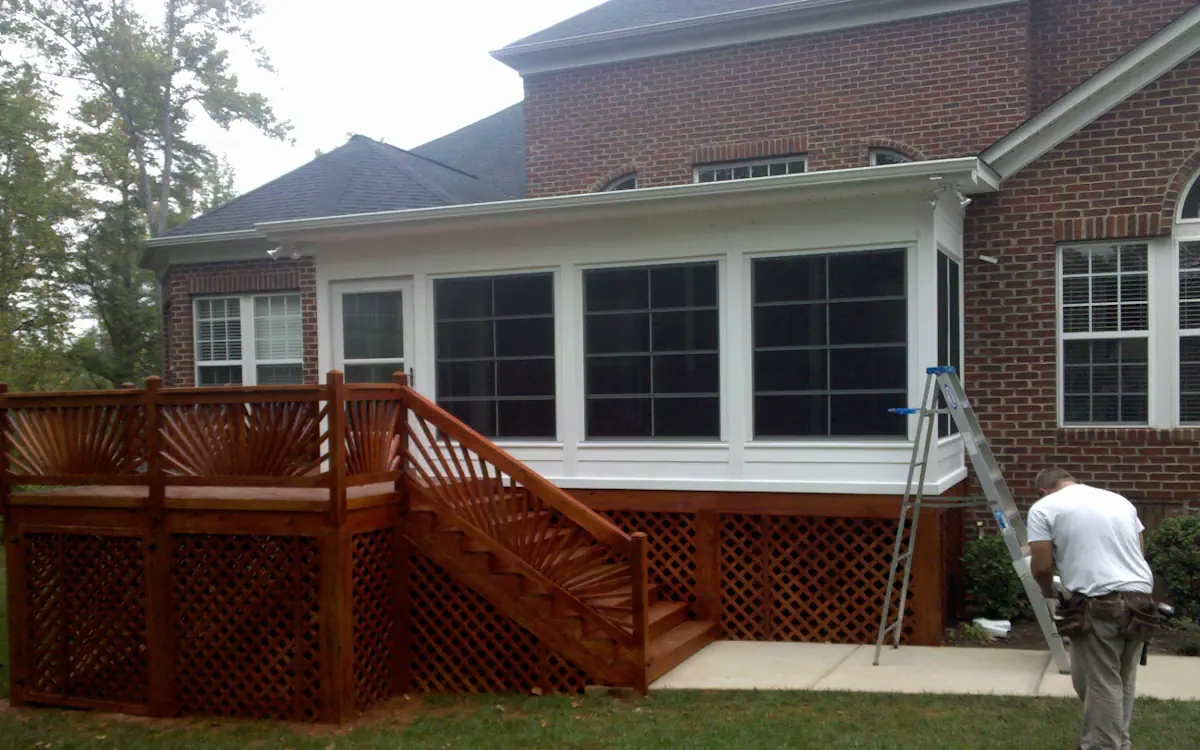 White sunroom with a flat roof, large grid-patterned sunroom windows, solid lower panels, and a single glass door for entry.
