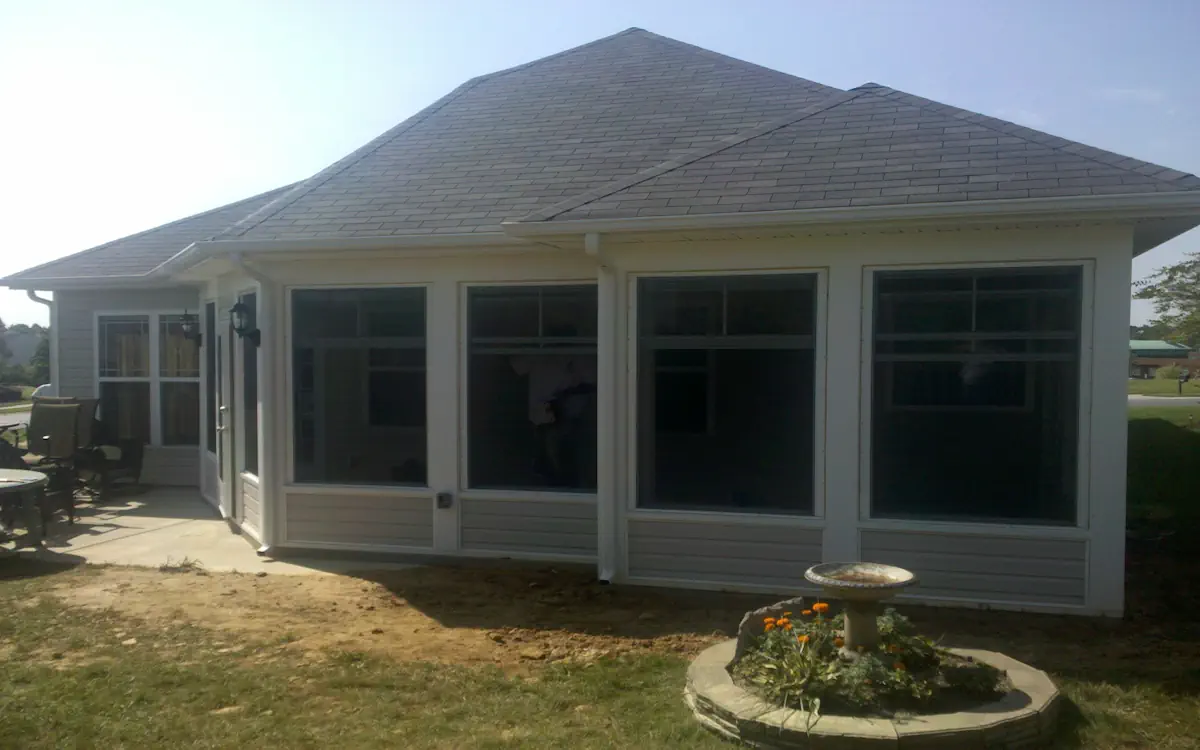 White sunroom with a hip roof, large sunroom windows with upper transoms, solid lower panels, and a glass door for entry.