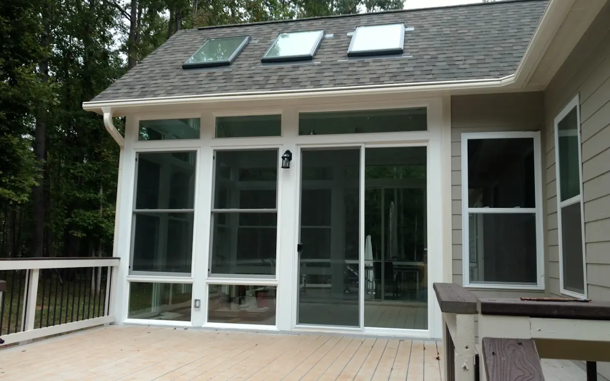 White sunroom with a gabled roof, three skylights, large sunroom windows with upper transoms, and a sliding glass door for entry.