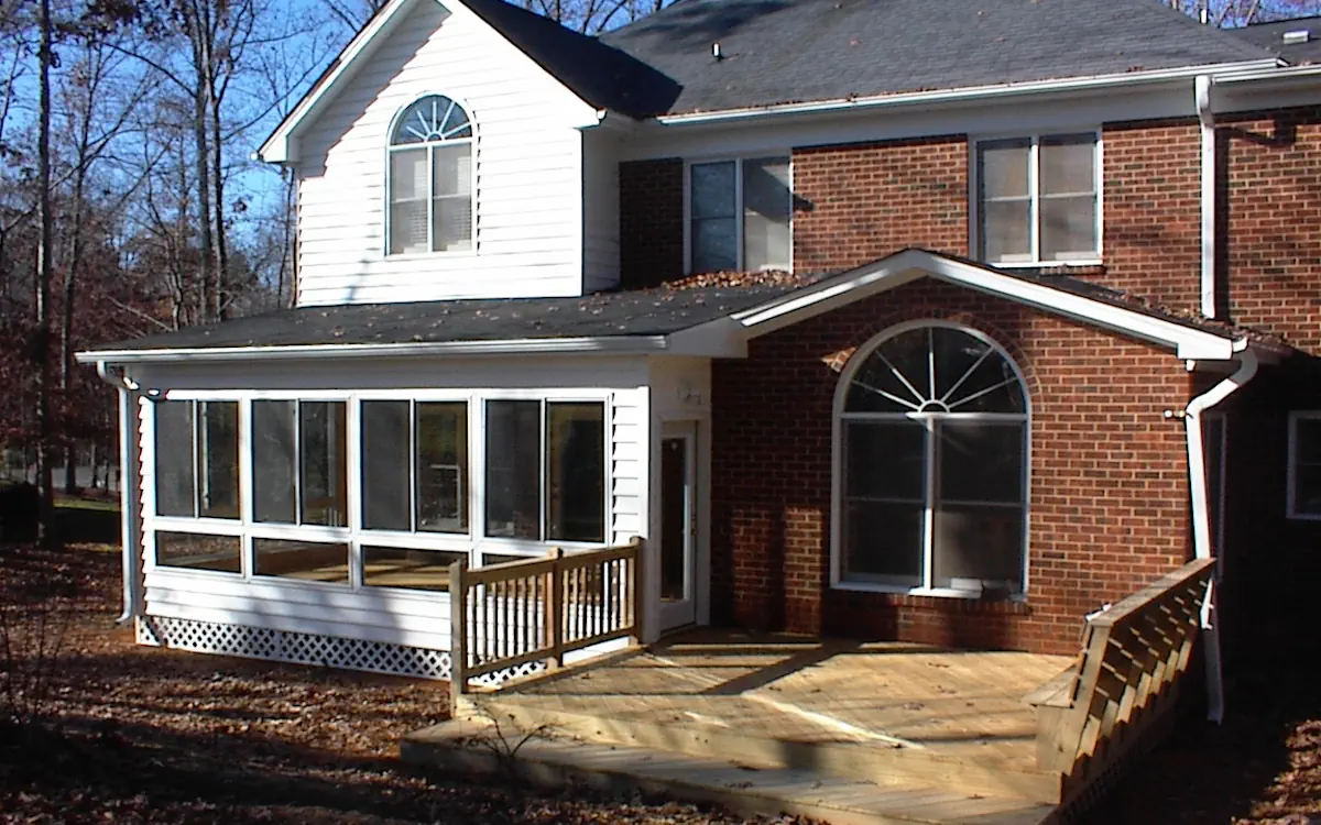 White sunroom with large sunroom windows, solid lower panels, lattice skirting, and an integrated entry door connecting to a wooden deck.
