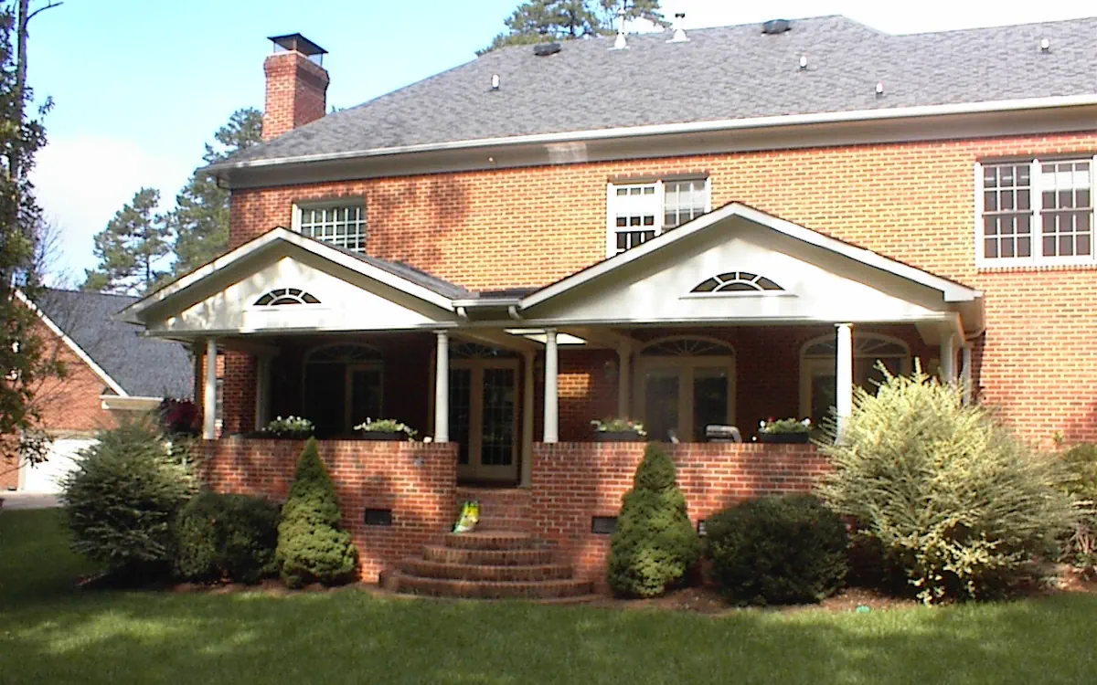 Covered porch has dual gabled roofs supported by white columns, complementing the brick exterior. A raised brick wall with built-in planters encloses the space.