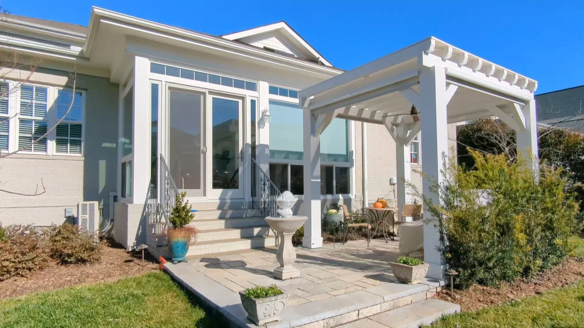 White sunroom with large glass doors, transom windows, elevated entry stairs with wrought iron railings, and a seamless connection to the home’s exterior.