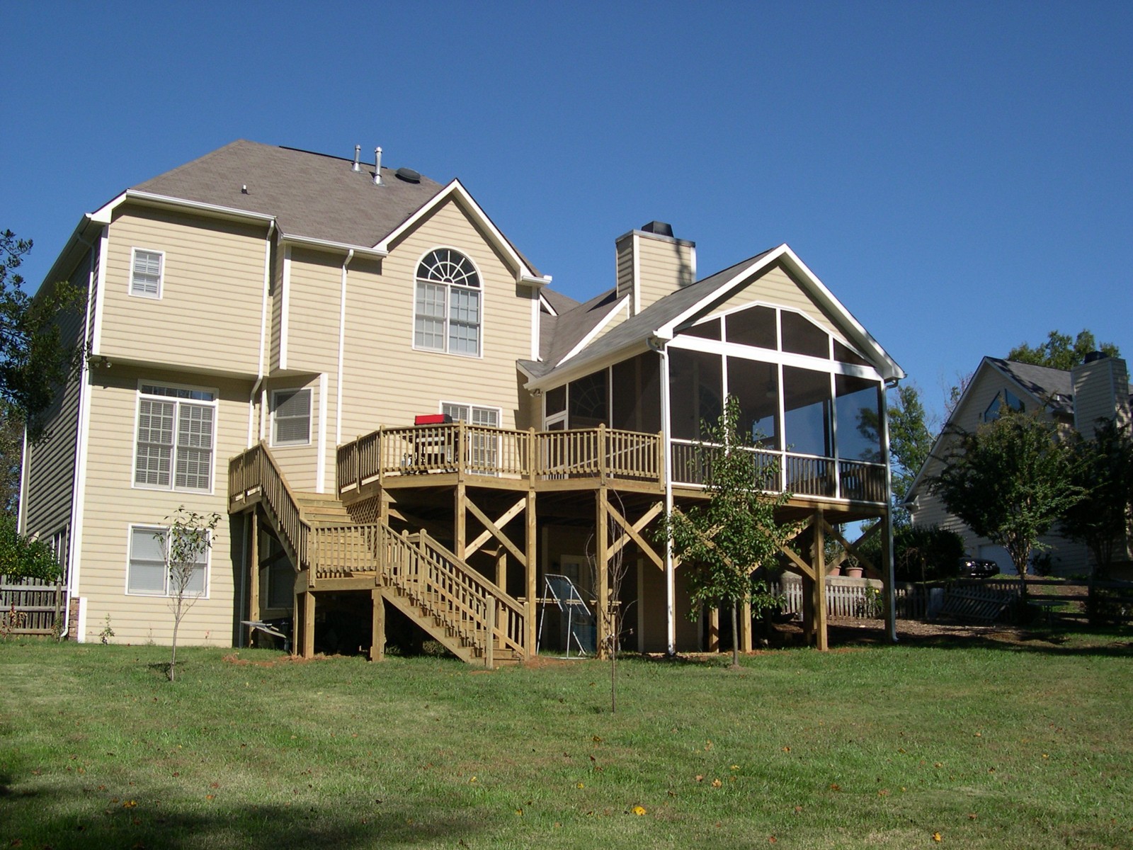 Completed elevated screened porch with a gable roof, adjoining wood deck and stairs to the lawn.
