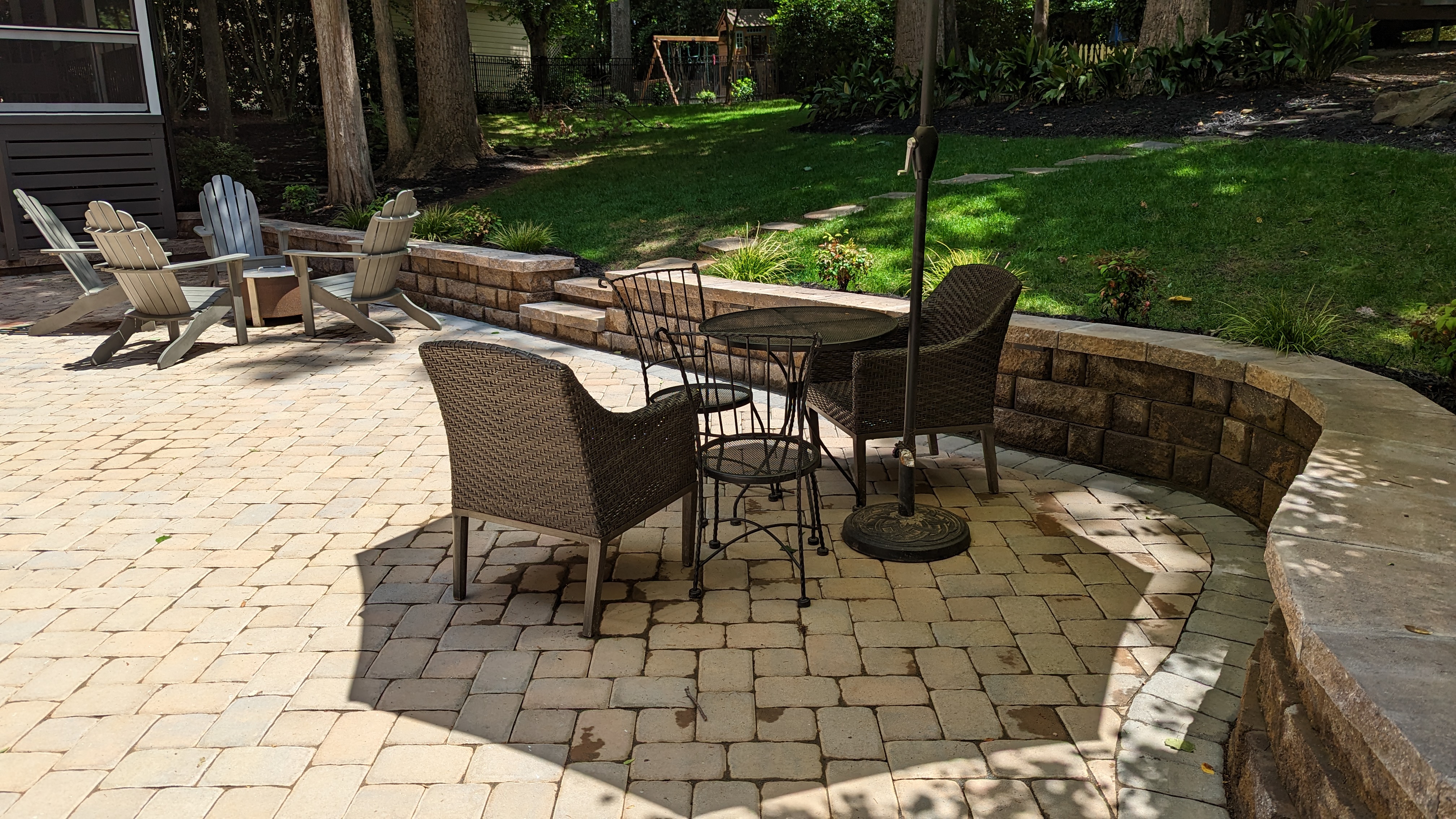 A curved retaining wall with integrated lighting defines the stone paver patio, with steps connecting to the lawn.