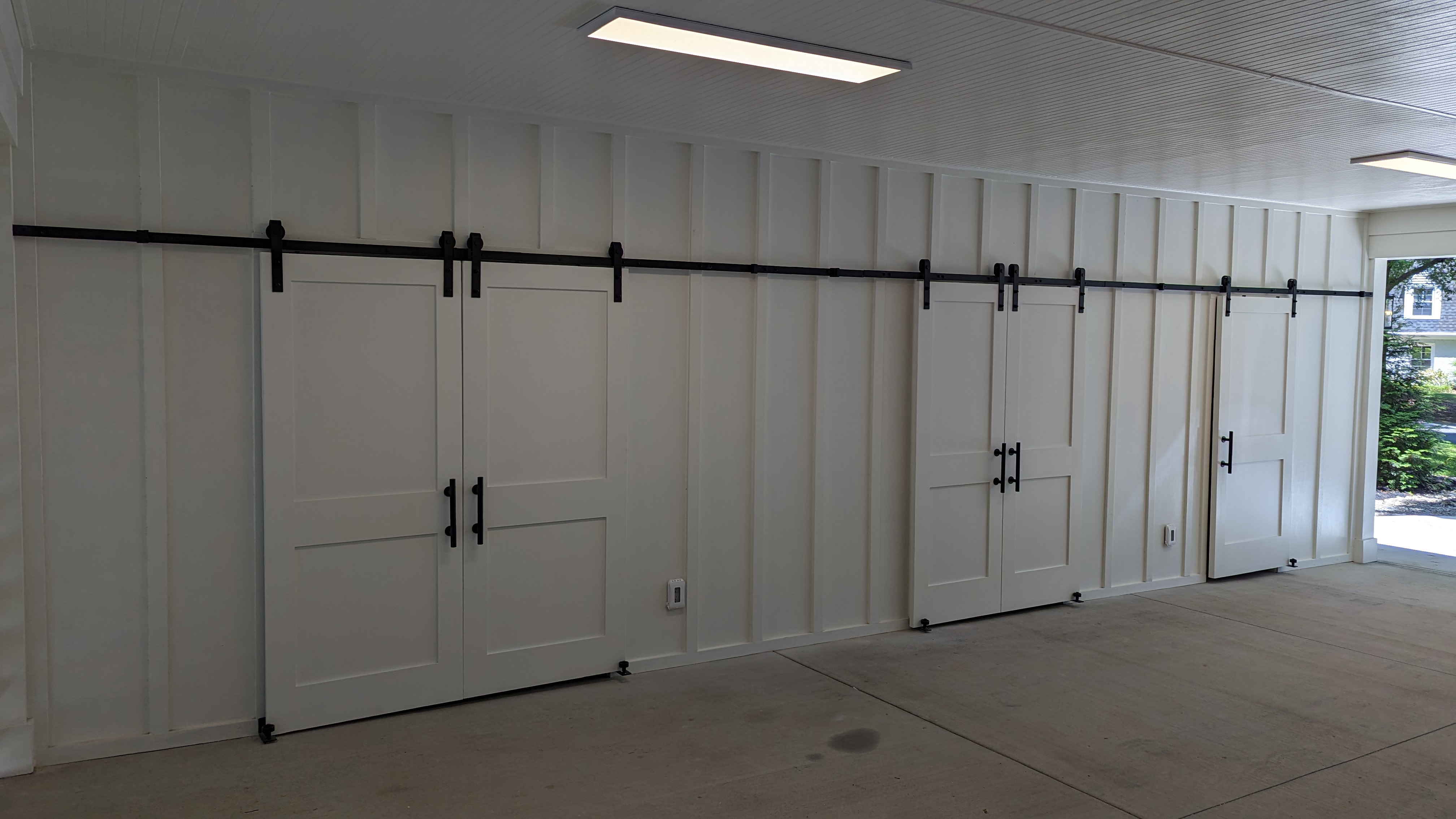 Sliding barn doors on exposed hardware conceal storage along the side of the carport.