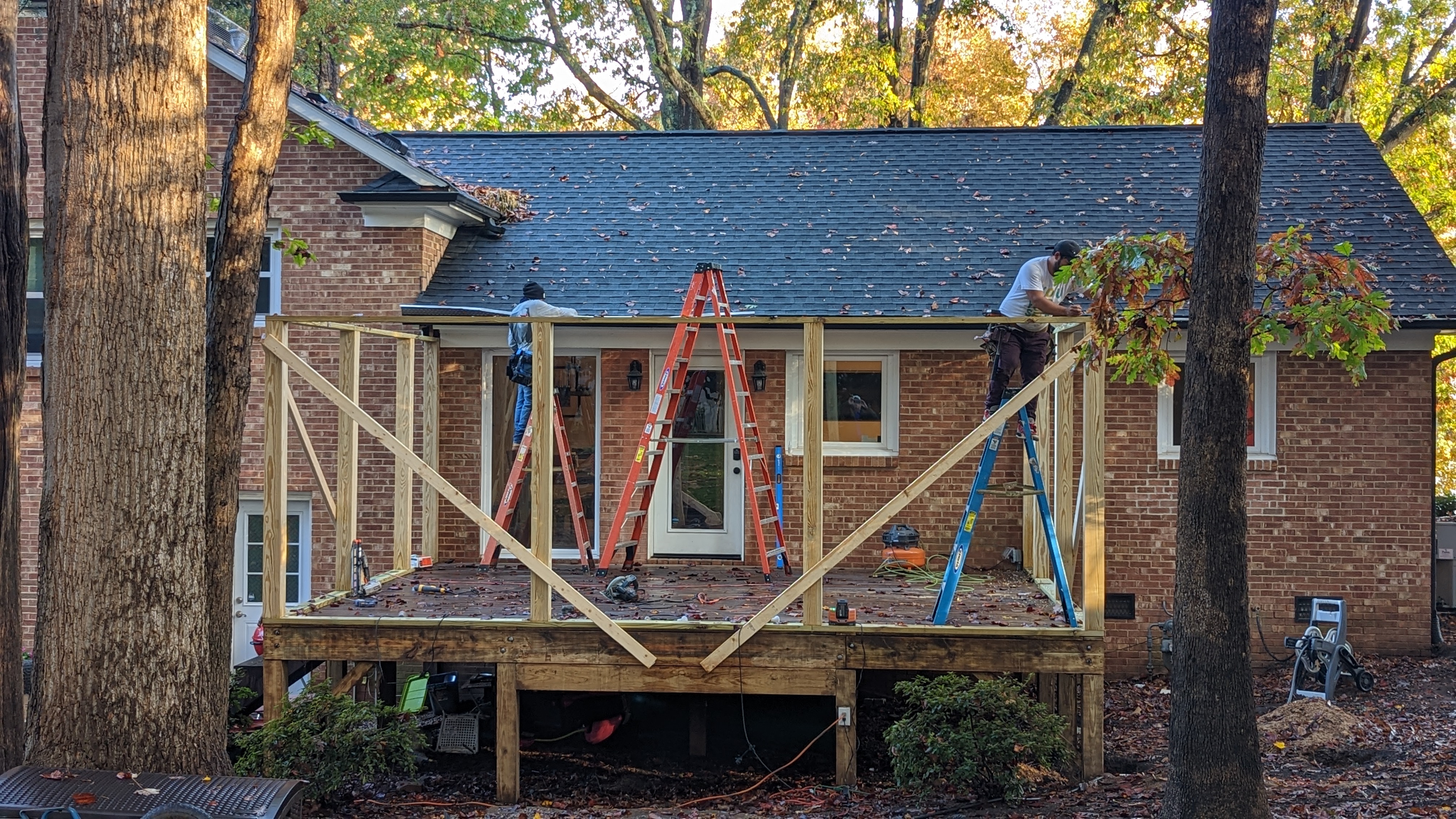 Early porch framing establishes the new outdoor room against the existing brick house.