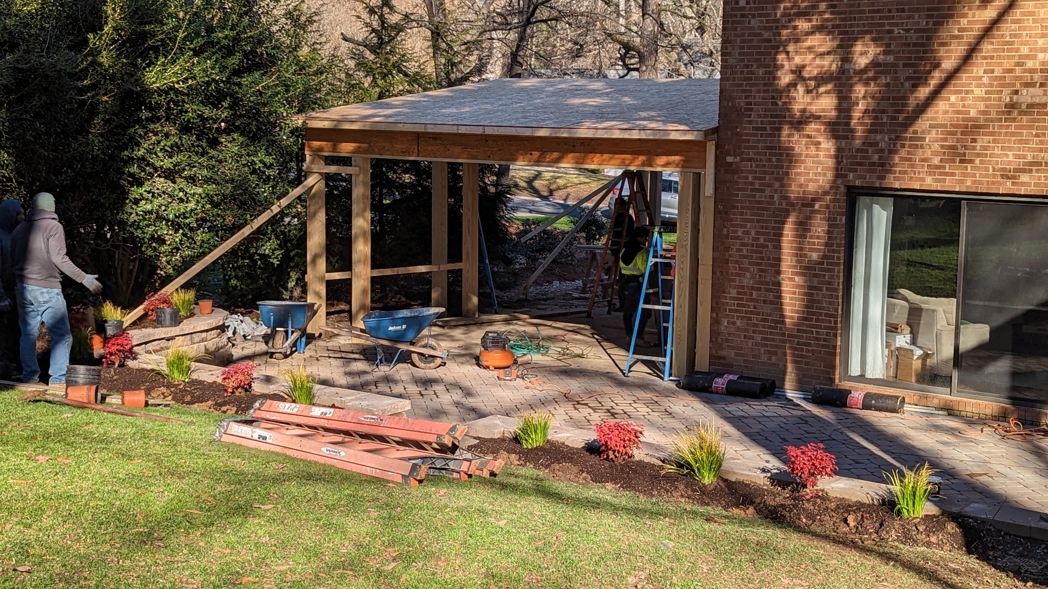 Roof sheathing covers the carport while temporary bracing supports the frame.