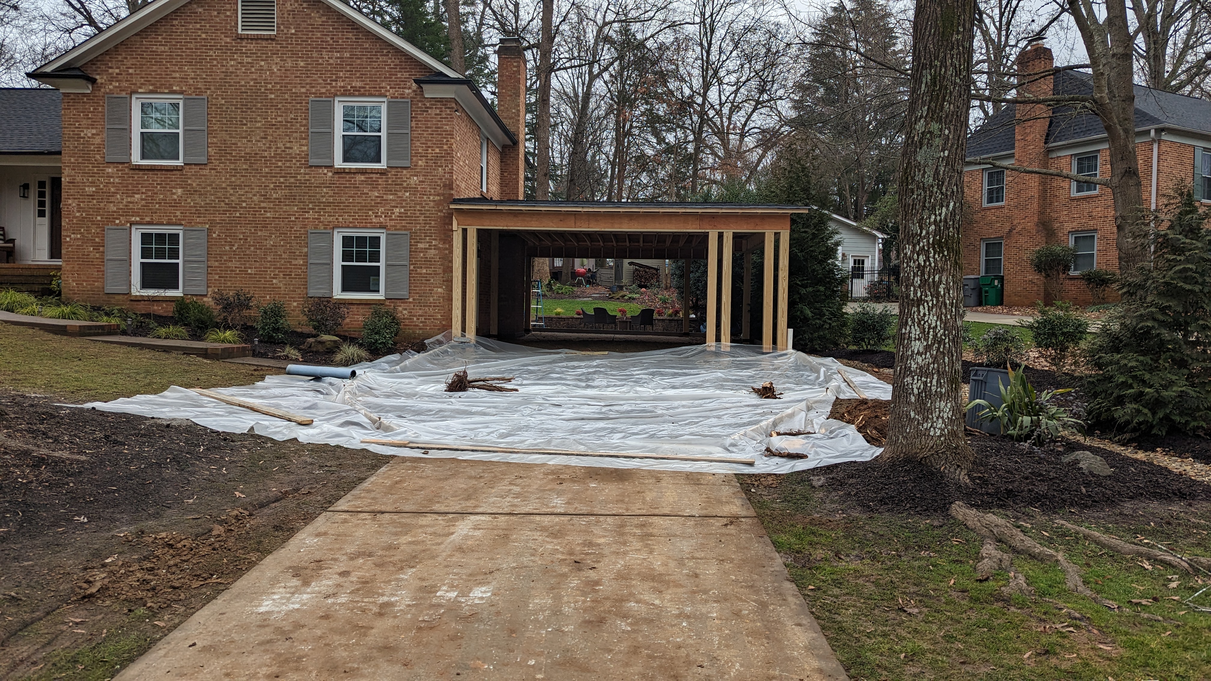 The front view shows the framed carport and preparations for the new driveway.