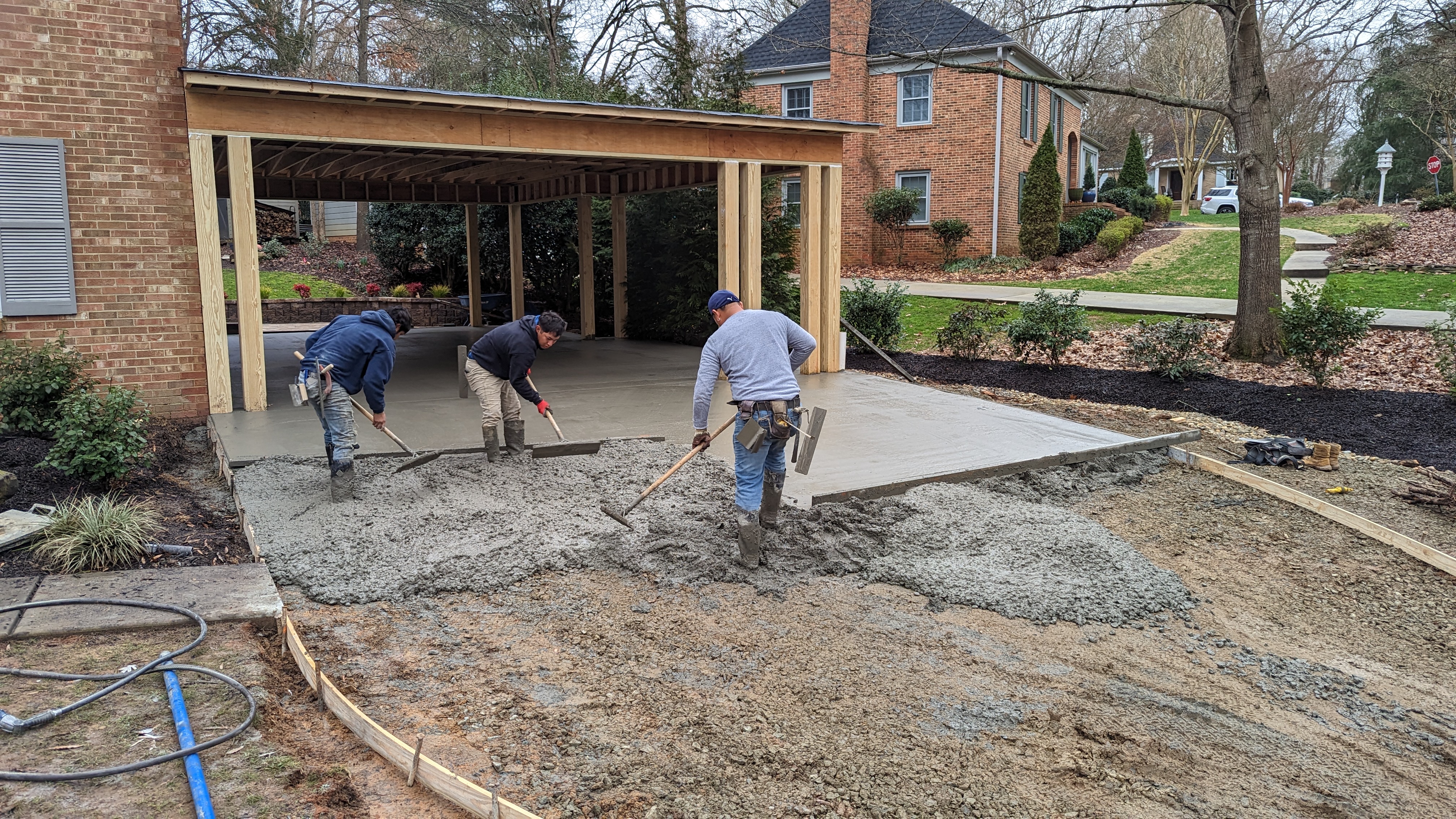 The concrete crew places and levels the new driveway in front of the carport.
